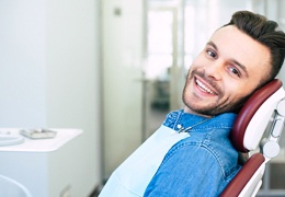 A male patient smiling while seated in a dentist’s chair preparing for his checkup with a Delta Dental dentist in Greater Inwood, Houston