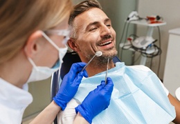A male patient sitting back in a dentist’s chair and smiling while a dental hygienist prepares to perform a cleaning