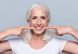 Older woman with dentures pointing to her teeth