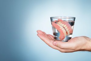 Hand holding glass of water with dentures